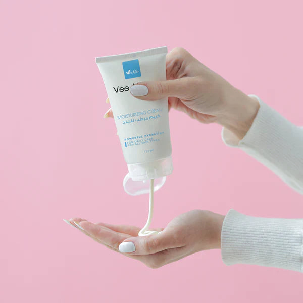 Vee Allure Moisturizing Cream tube dispensing cream on hand against pink background